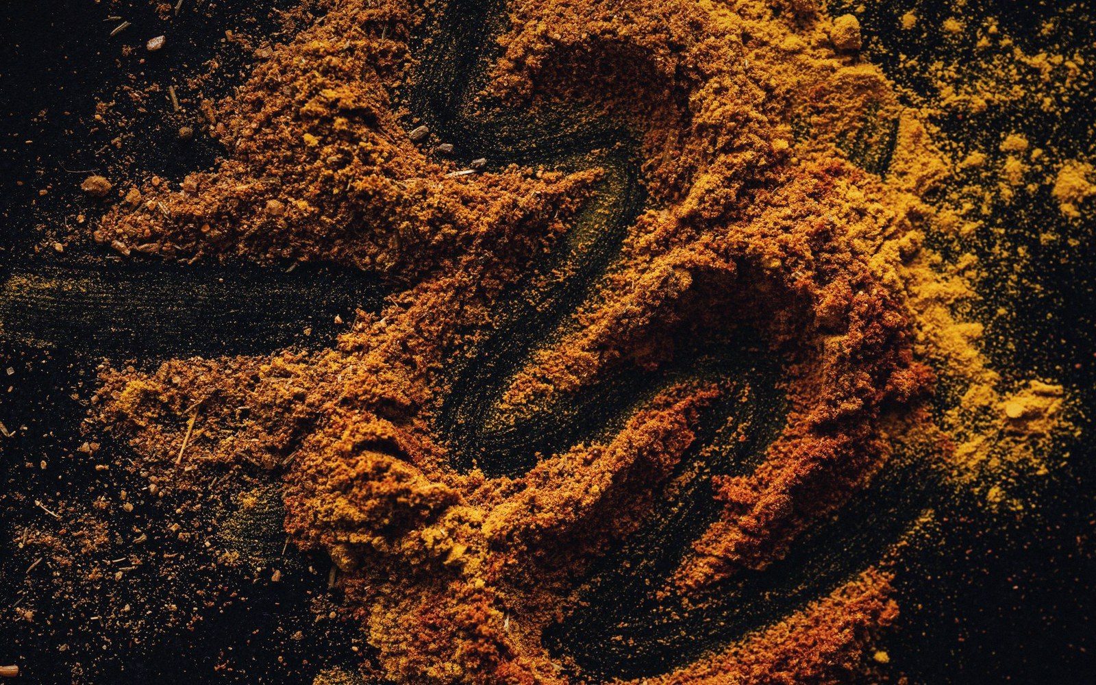 Swirled patterns of orange and brown spice powder on a dark surface