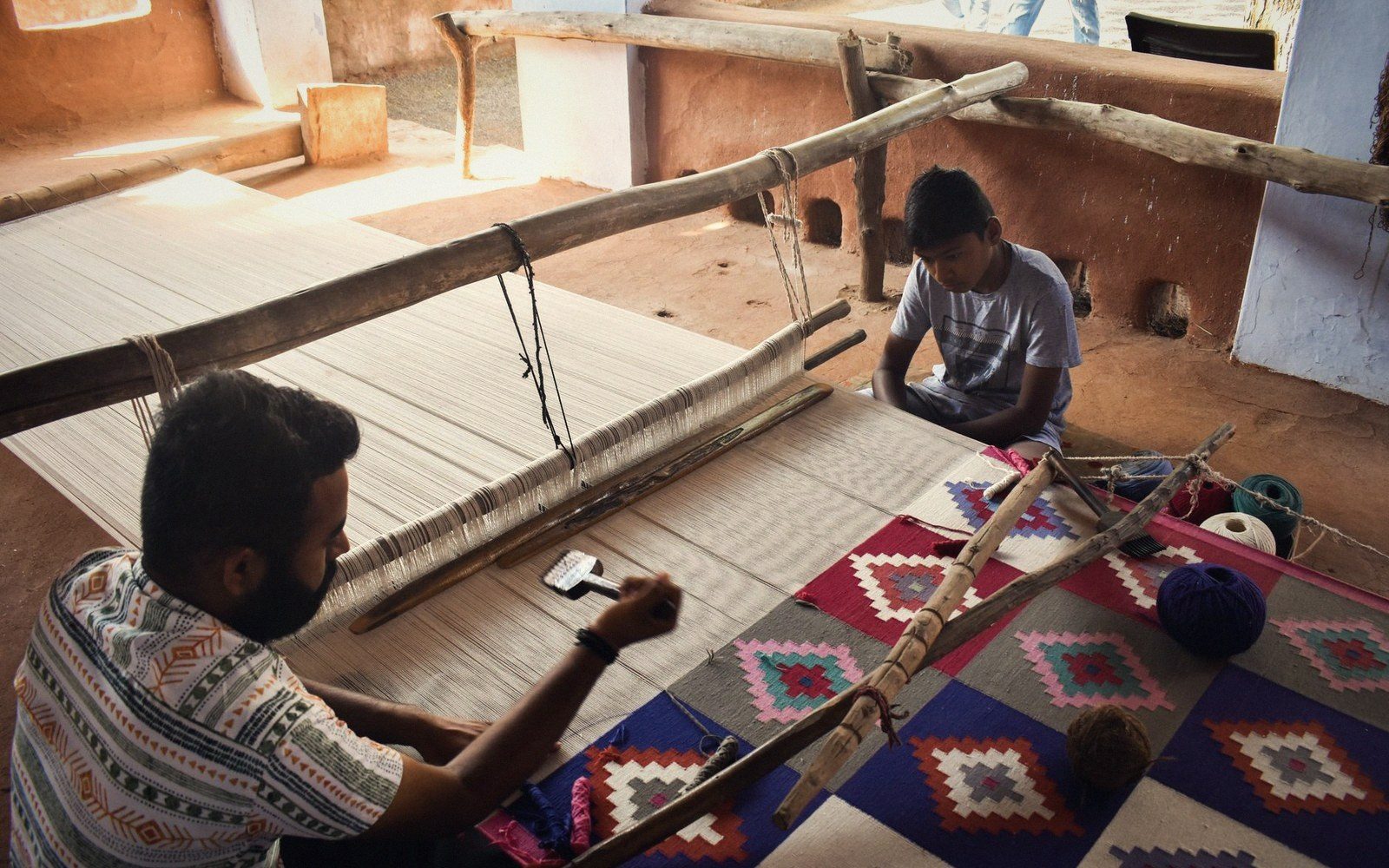 Two weavers work a traditional handloom weaving a patterned textile in a rural workshop
