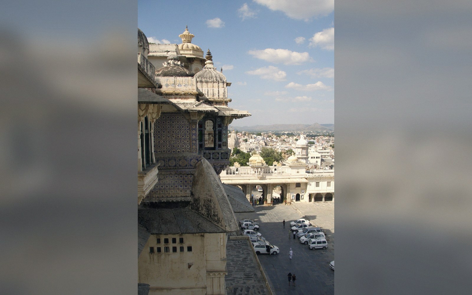 Ornate domed balcony overlooks a courtyard and parked cars with the city skyline beyond